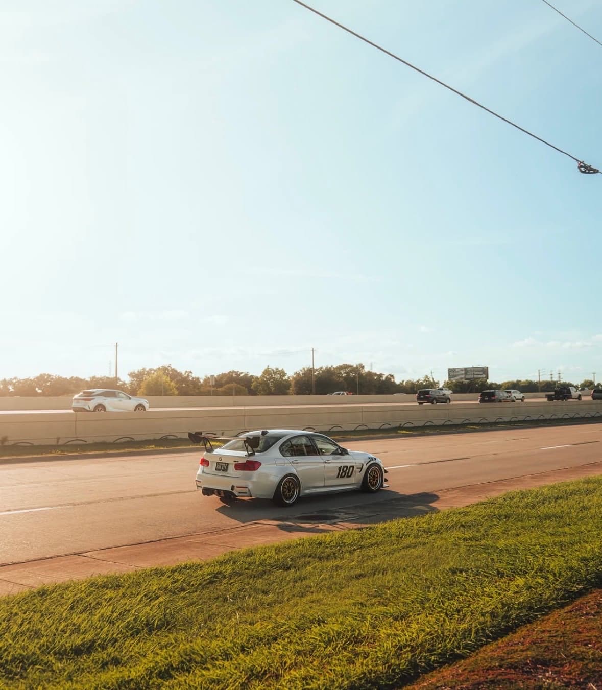 White BMW M3 track car with a rear wing on the road at golden hour