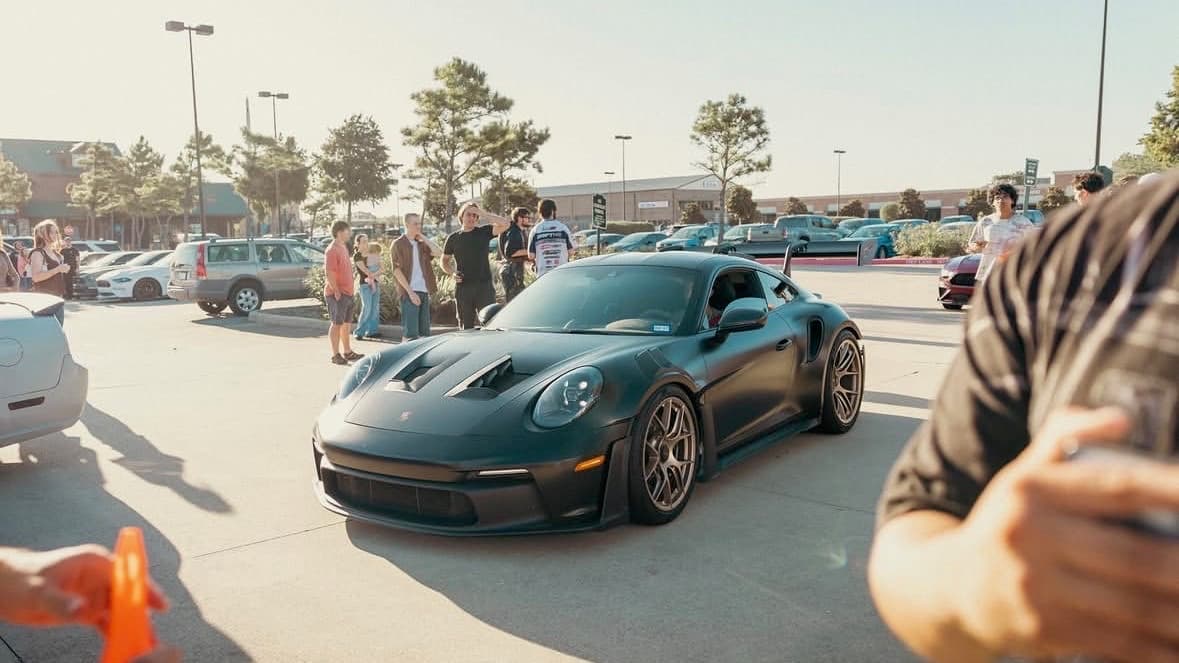 Dark green Porsche 911 GT3 RS rolling into a BL4NK meet as the crowd watches